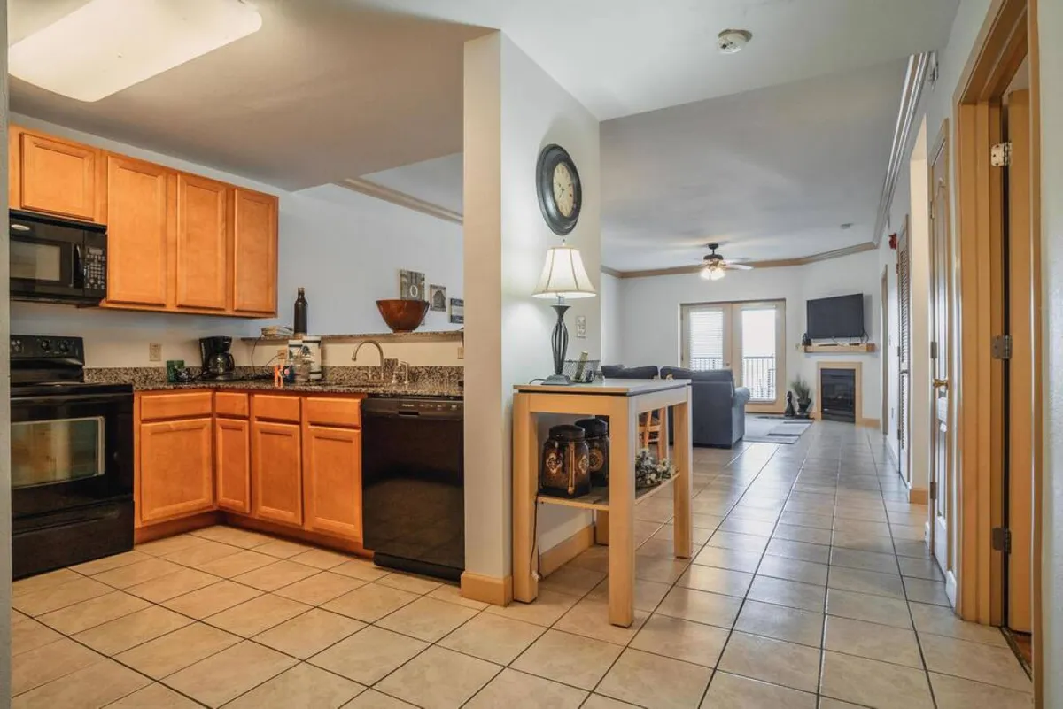 A view connecting the kitchen and living room, featuring warm cabinetry, a practical countertop, fireplace, and a glimpse of the balcony. The layout is open and accessible, reflecting the inclusive, wheelchair-friendly design described in the section.