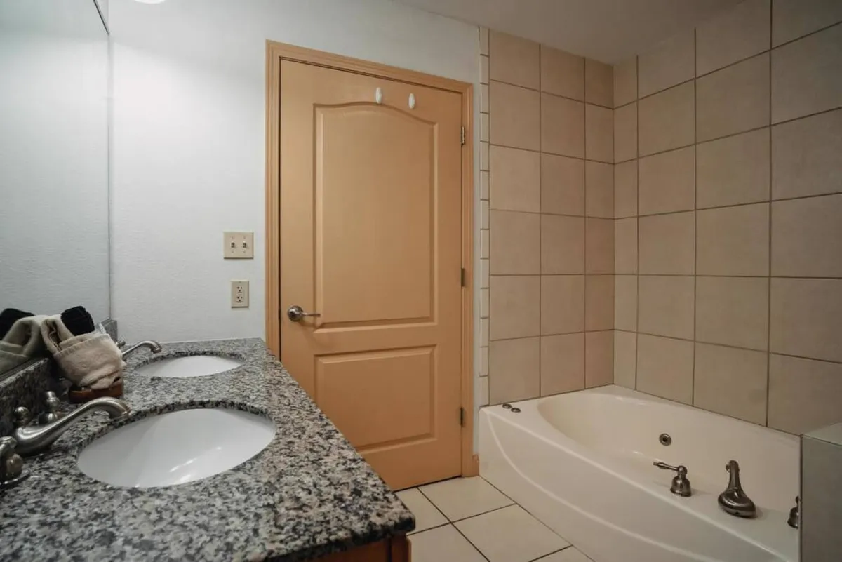 A serene bathroom showcasing double vanity sinks, a spacious granite countertop, and a luxurious bathtub—perfect for indulging in a soothing soak after a busy day. The neutral tones and clean lines evoke a spa-like ambiance.