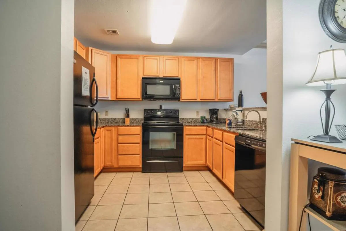 A warmly lit kitchen featuring a spacious granite island, black appliances, and wooden cabinets. The setup is inviting for cooking, baking, and gathering, with ample space for preparing family meals or entertaining guests.