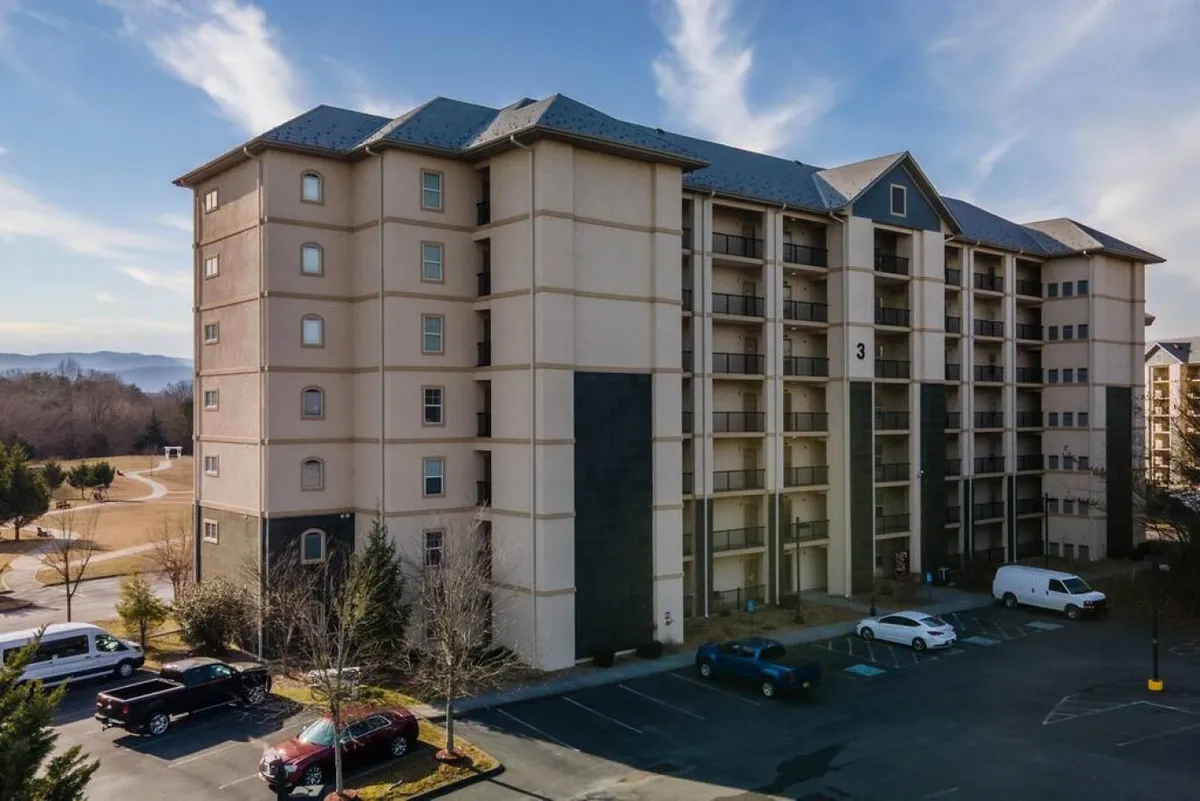 This image shows the exterior facade of the condo building with the parking lot in the foreground and a well-maintained landscape surrounding the property. The view suggests easy access for guests and a welcoming arrival experience.