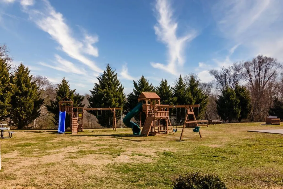 A cheerful exterior image of a colorful playground featuring a green slide, swing set, and open space for children to play. The environment radiates joy and is perfect for family gatherings or outdoor picnics.