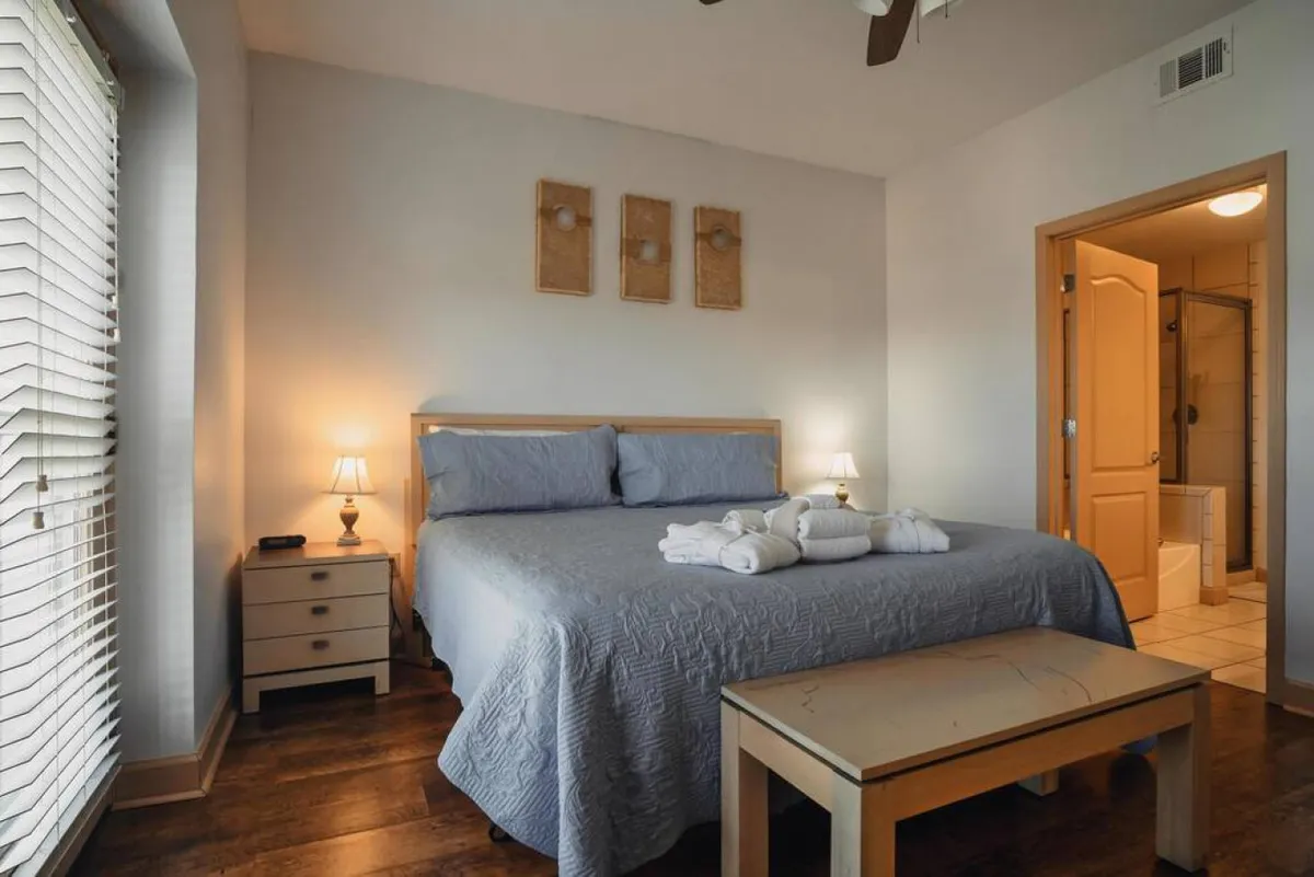 The image features a serene bedroom interior with a plush bed adorned in inviting blue bedding, complemented by warm table lamps and calming decorative wall art. The space exudes comfort, perfect for unwinding after a day exploring the mountains.