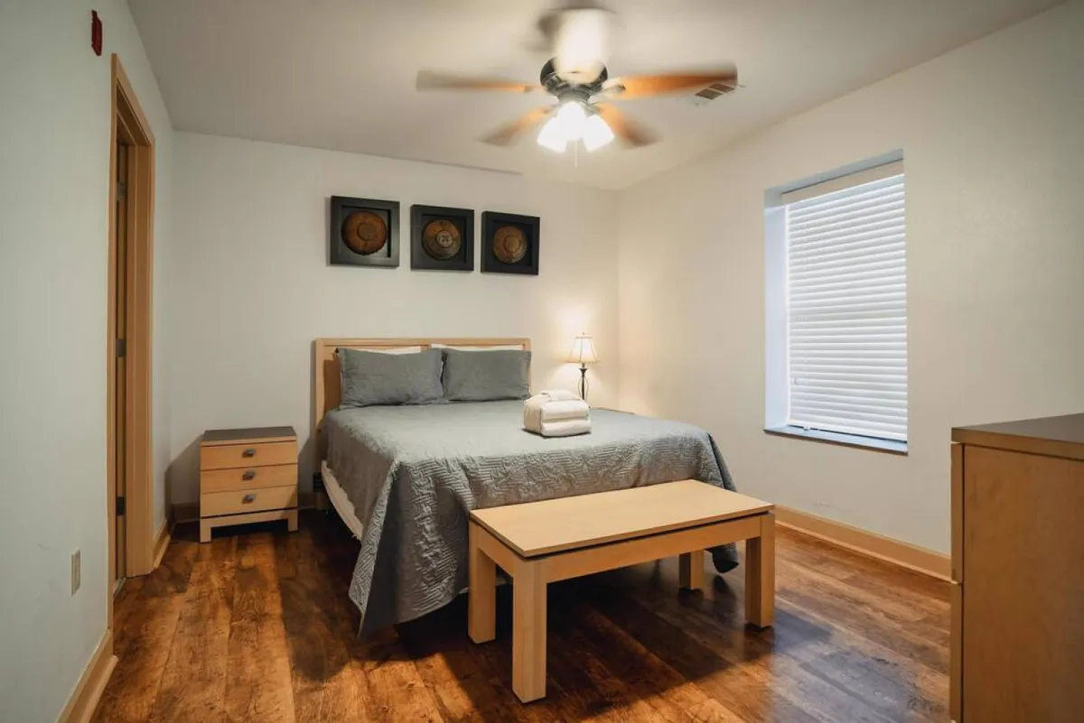 A cozy bedroom featuring a comfortable bed with fresh linens, a nightstand with a lamp perfect for reading, and artwork on the wall. The soft lighting and inviting decor evoke a sense of calm and relaxation, ideal for unwinding after a day of adventures.