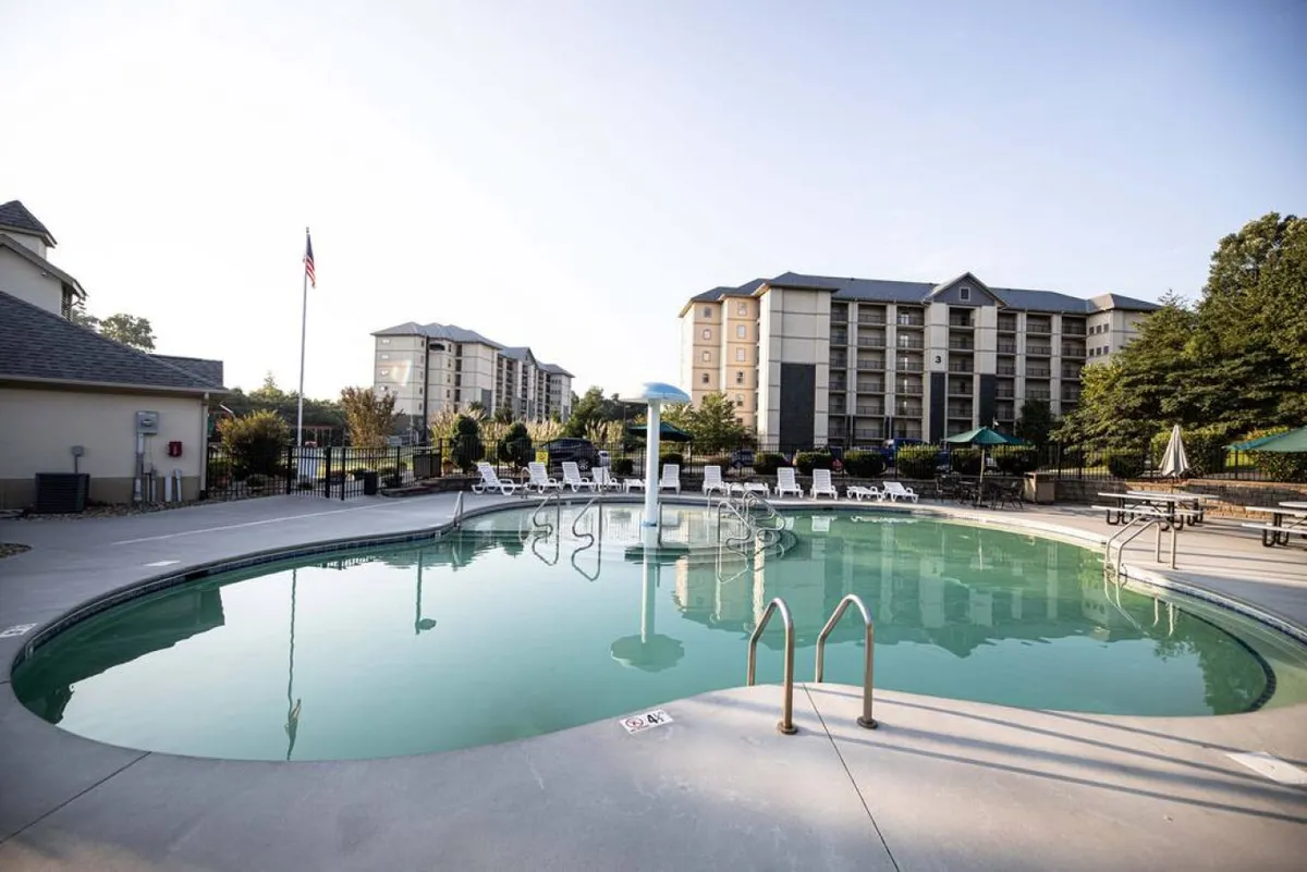 This exterior image showcases a large outdoor swimming pool surrounded by lounge chairs and lush greenery, with the building facade visible in the background. The inviting pool area communicates a fun, family-friendly atmosphere ideal for children and parents alike to relax and play outdoors.